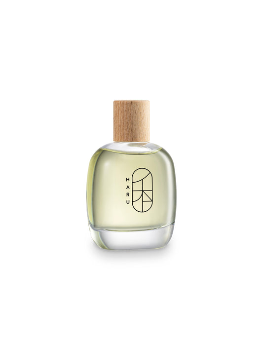 A clear glass bottle of HARU Eau de Parfum with a wooden cap, displaying the brand's logo on the front.