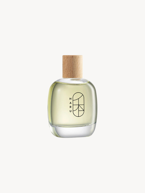 A clear glass bottle of HARU Eau de Parfum with a wooden cap, displaying the brand's logo on the front.