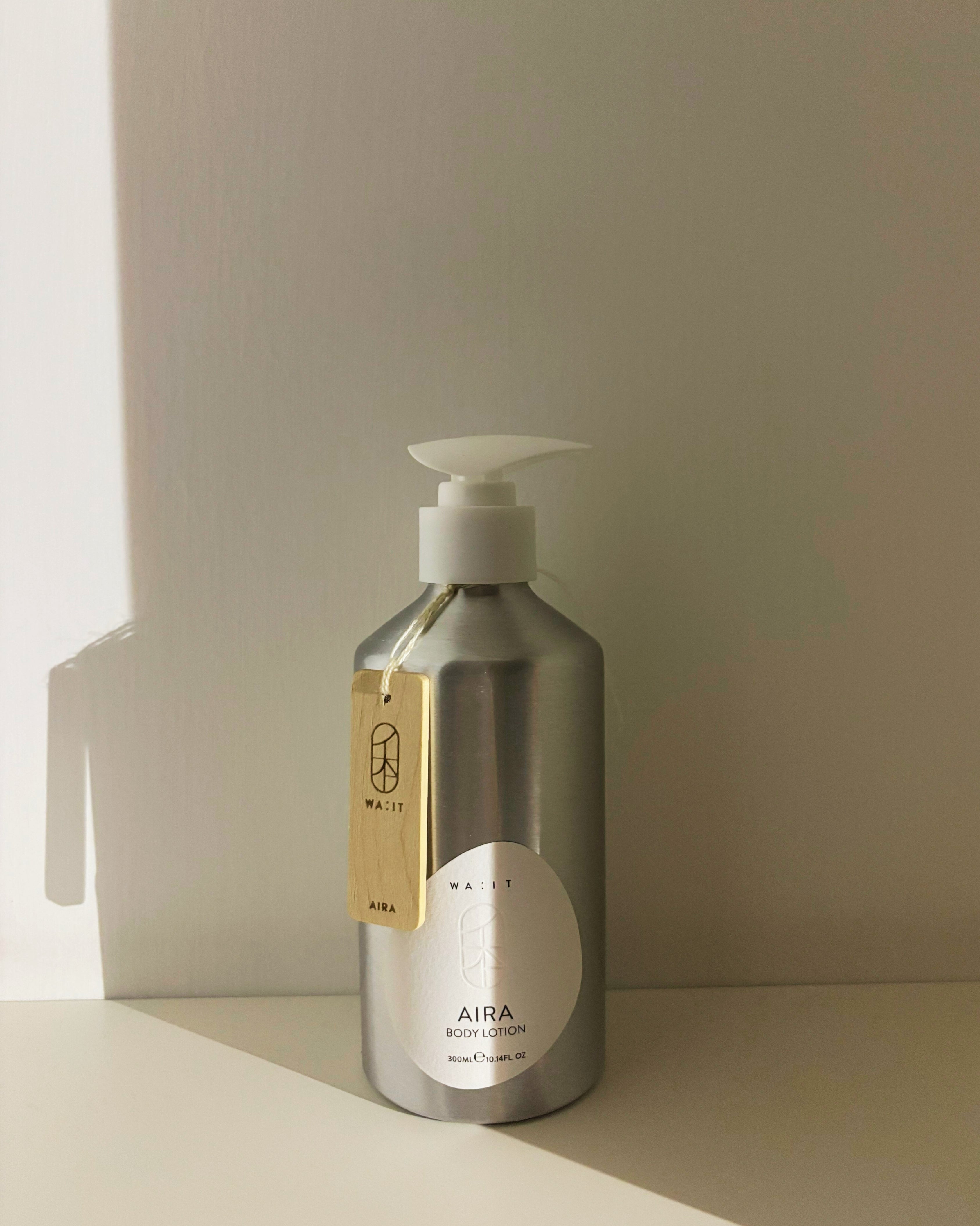 Silver bottle of 'AIRA' body lotion with a pump on a beige surface.
